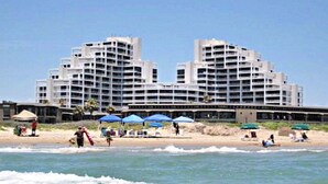 Ein Hotel direkt am Strand mit mehreren Etagen, Sitzgelegenheiten im Freien und Sonnenschirmen.