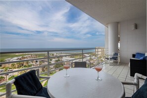 Ein Balkon mit Tisch und Stühlen, der auf einen Strand und einige Gebäude blickt.