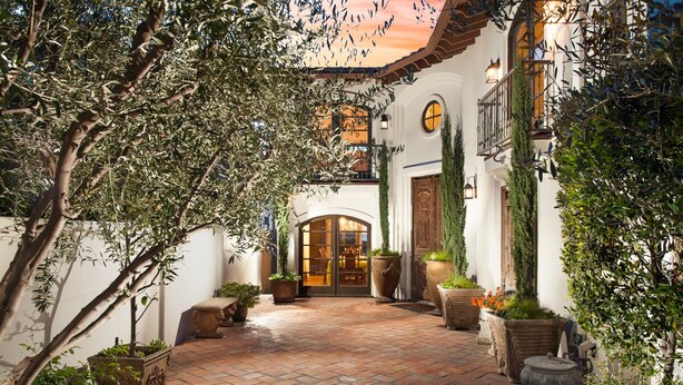 A courtyard with a tiled floor, potted plants, and a building with a wooden door and windows. - Gorgeous Spanish-style Home with Stunning Ocean Views. New Stil™ jacuzzi! (Newport Beach)