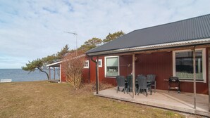 A red wooden house with a covered patio, a table and chairs, and a view of the sea. - 2 bedroom pet friendly home in Visby (Visby)