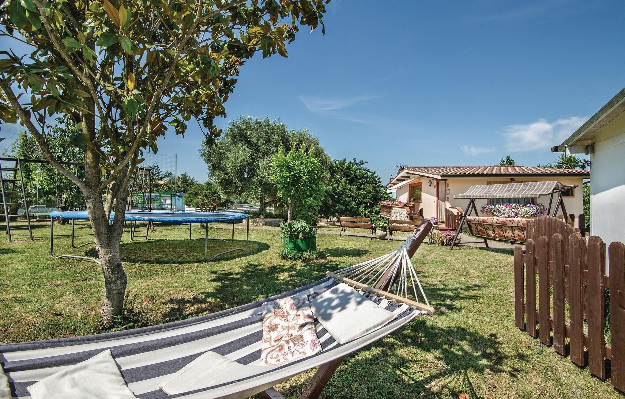 Un'amaca in un giardino erboso, con una casa e un trampolino sullo sfondo.