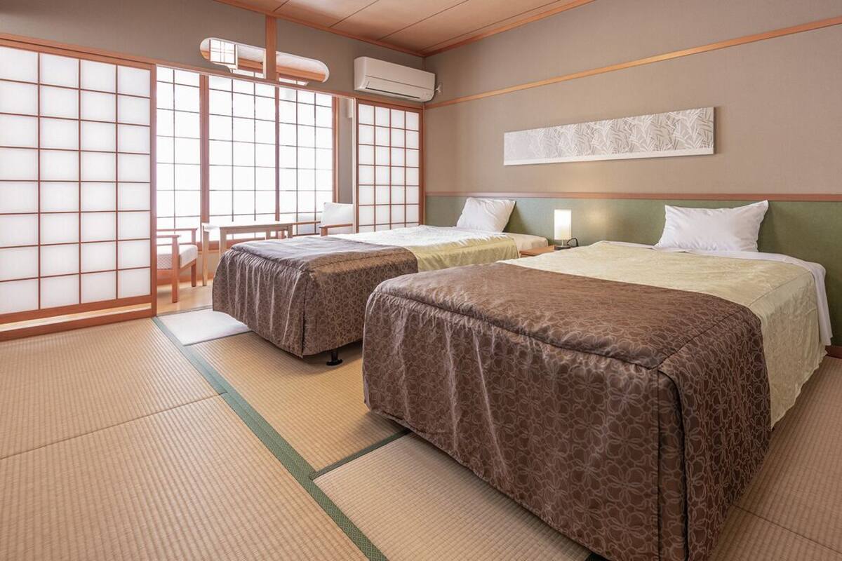 A traditional Japanese-style room with tatami flooring, two beds, a shoji screen, and a futon.