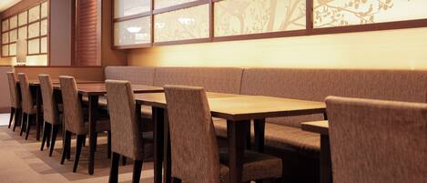 Un restaurant avec une longue table en bois et des chaises rembourrées, un mur bas agrémenté d’un panneau décoratif et un sol recouvert de moquette.