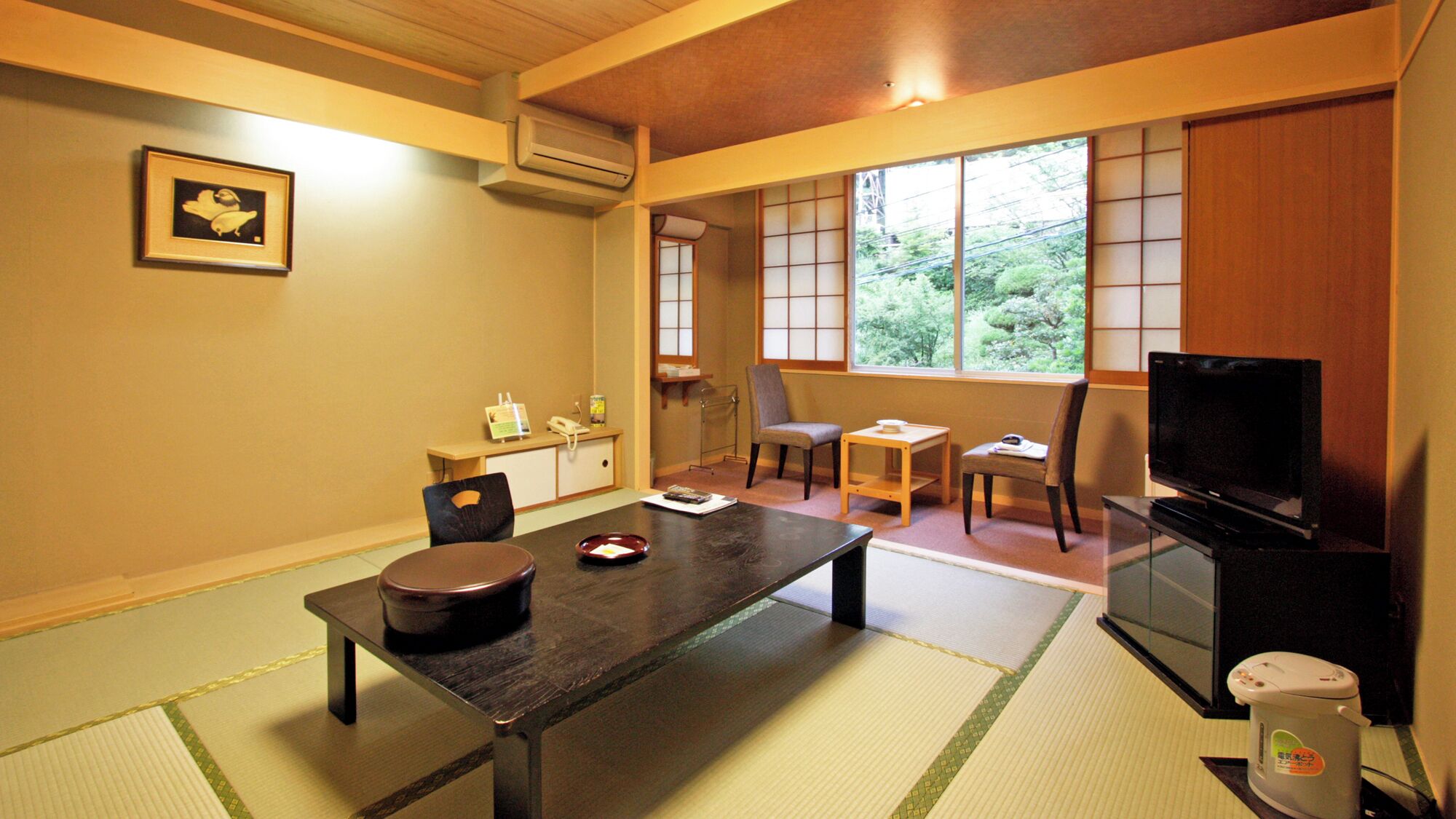 Een traditionele Japanse kamer met tatami vloeren, een lage tafel met een donker houten blad, een televisie en een schuifdeur naar uitzicht op groen.