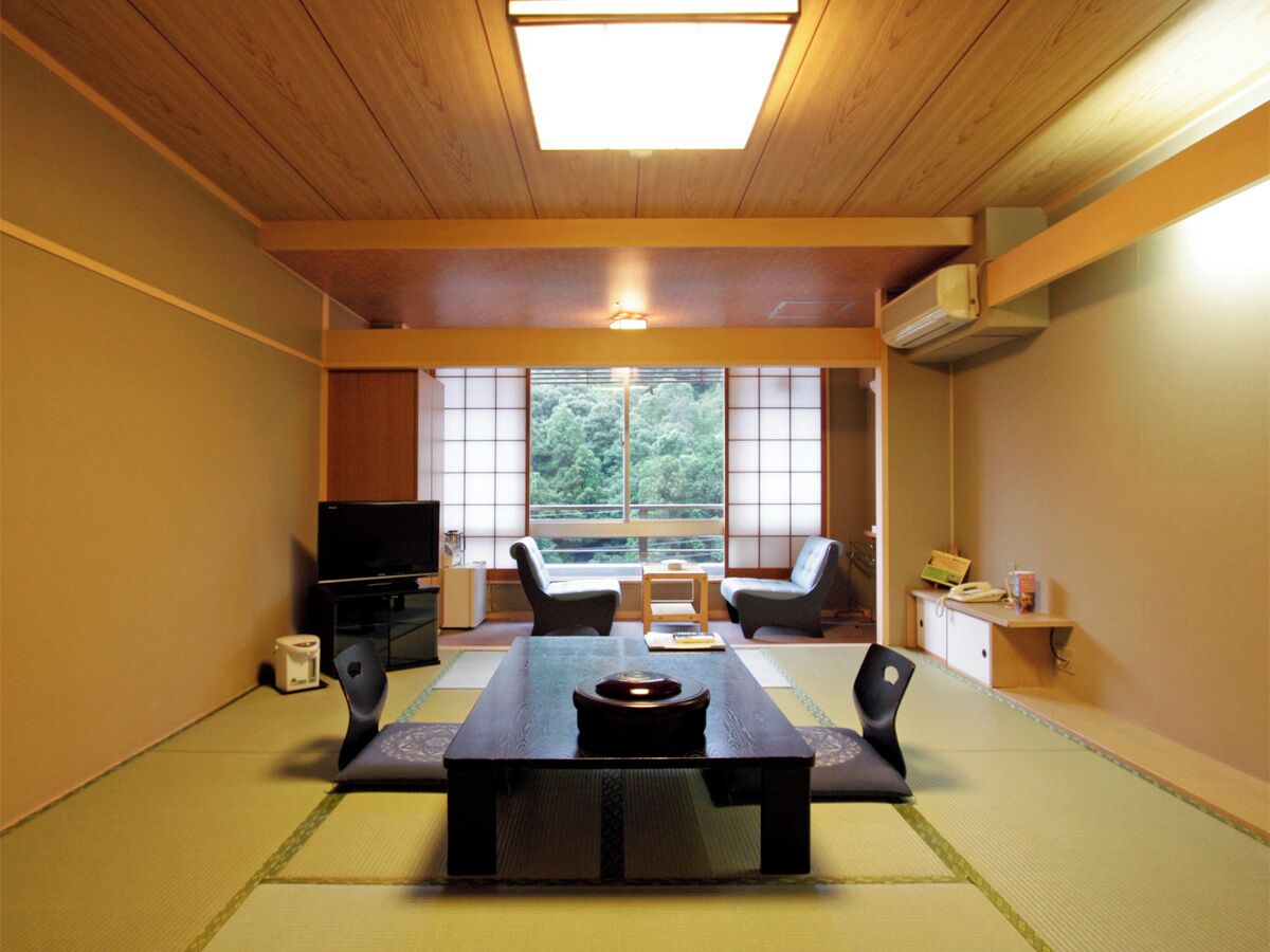 Een traditionele Japanse kamer met tatami vloerbedekking, een lage tafel, twee stoelen, een televisie en een schuifdeur naar een balkon.
