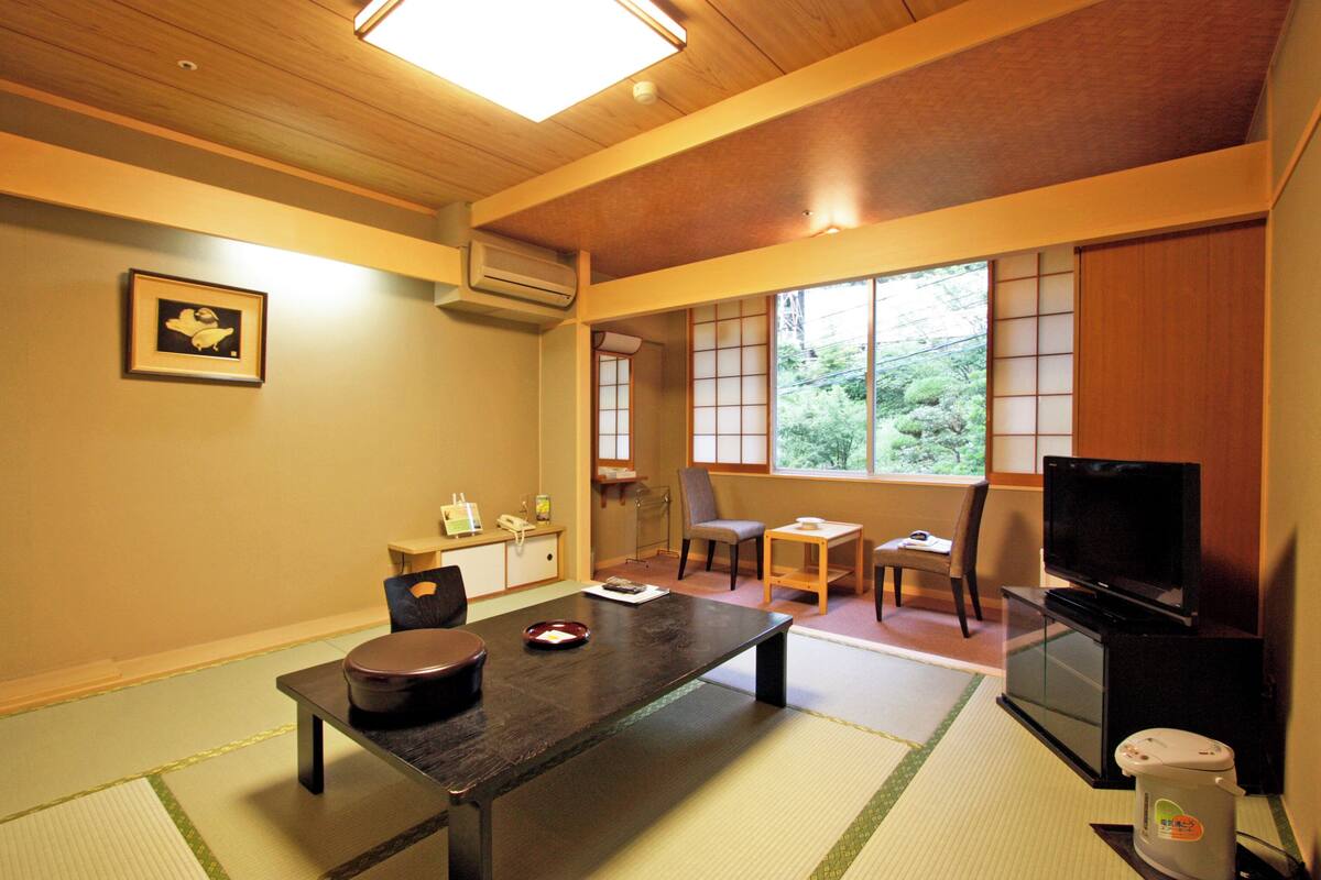 A traditional Japanese room with tatami flooring, a low table, a television, and a futon bed.