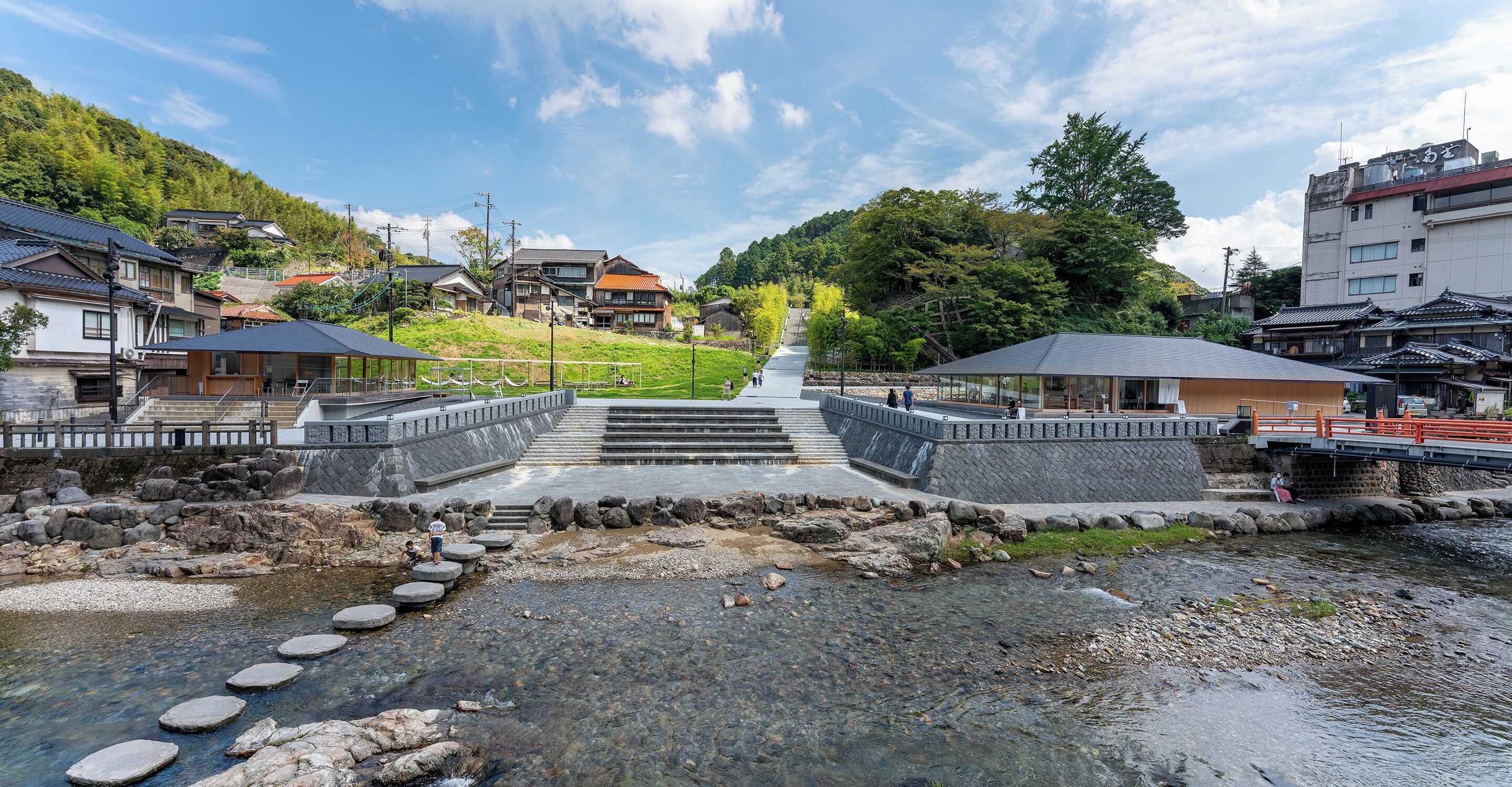 Eine traditionelle japanische Stadt mit Steinstufen, die zu einem Fluss führen, umgeben von Wohnhäusern und Grünflächen.