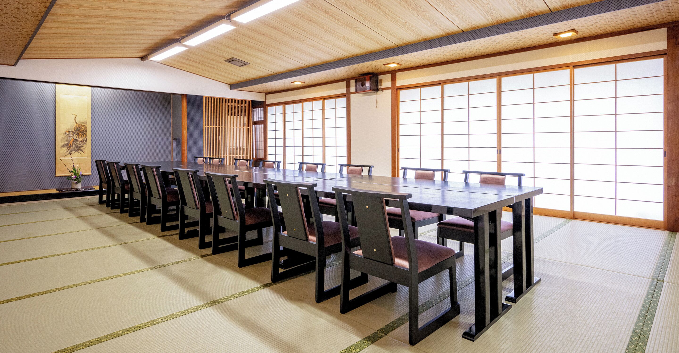 A conference room with a long table and chairs, large windows, and tatami mat flooring.