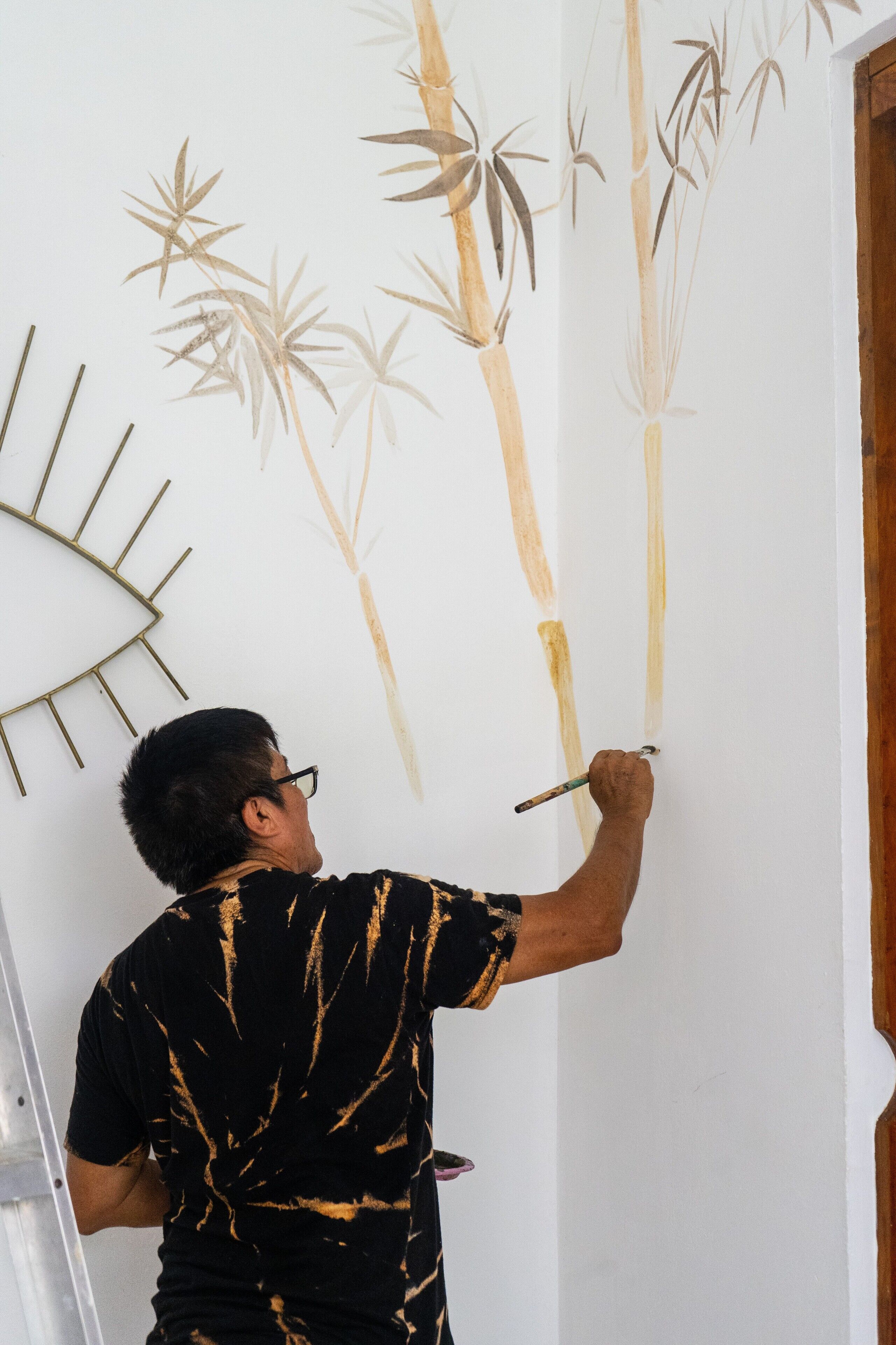 A person painting a wall with bamboo designs.