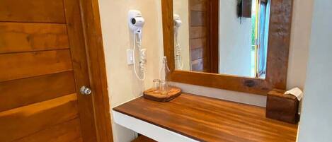A bathroom with a wooden vanity, a mirror, a hairdryer, and a towel rack.