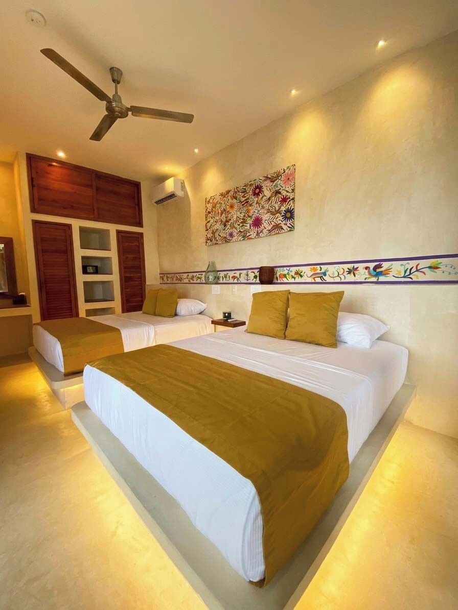A hotel room with two beds, a ceiling fan, a wall-mounted air conditioner, and a decorative wall piece.