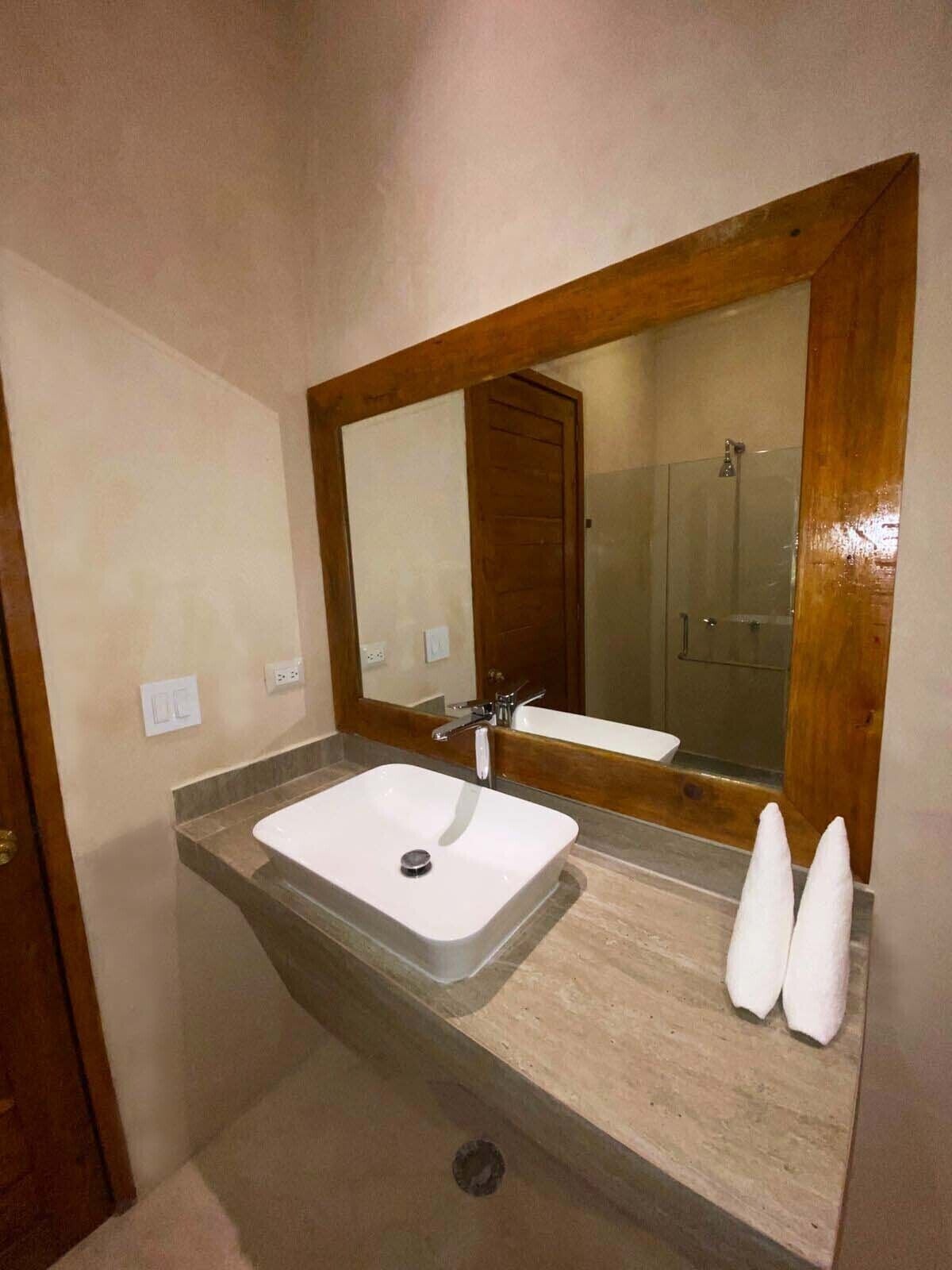 Een badkamer met een rechthoekig wastafel, een grote spiegel en een douche die in de spiegeling te zien is.