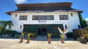 Un hotel llamado MAJO con techo de paja, un letrero y plantas en macetas en la entrada.