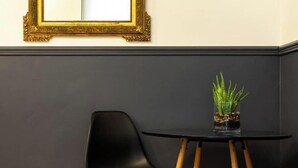 A room with a black chair, a small table with a plant, and a gold-framed mirror on the wall. - MAGNIFICENT APARTMENT NEAR THE EIFFEL TOWER (Paris)
