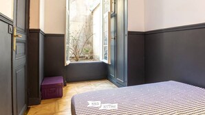 A bedroom with a bed, a window, a door, and a small purple suitcase. - MAGNIFICENT APARTMENT NEAR THE EIFFEL TOWER (Paris)