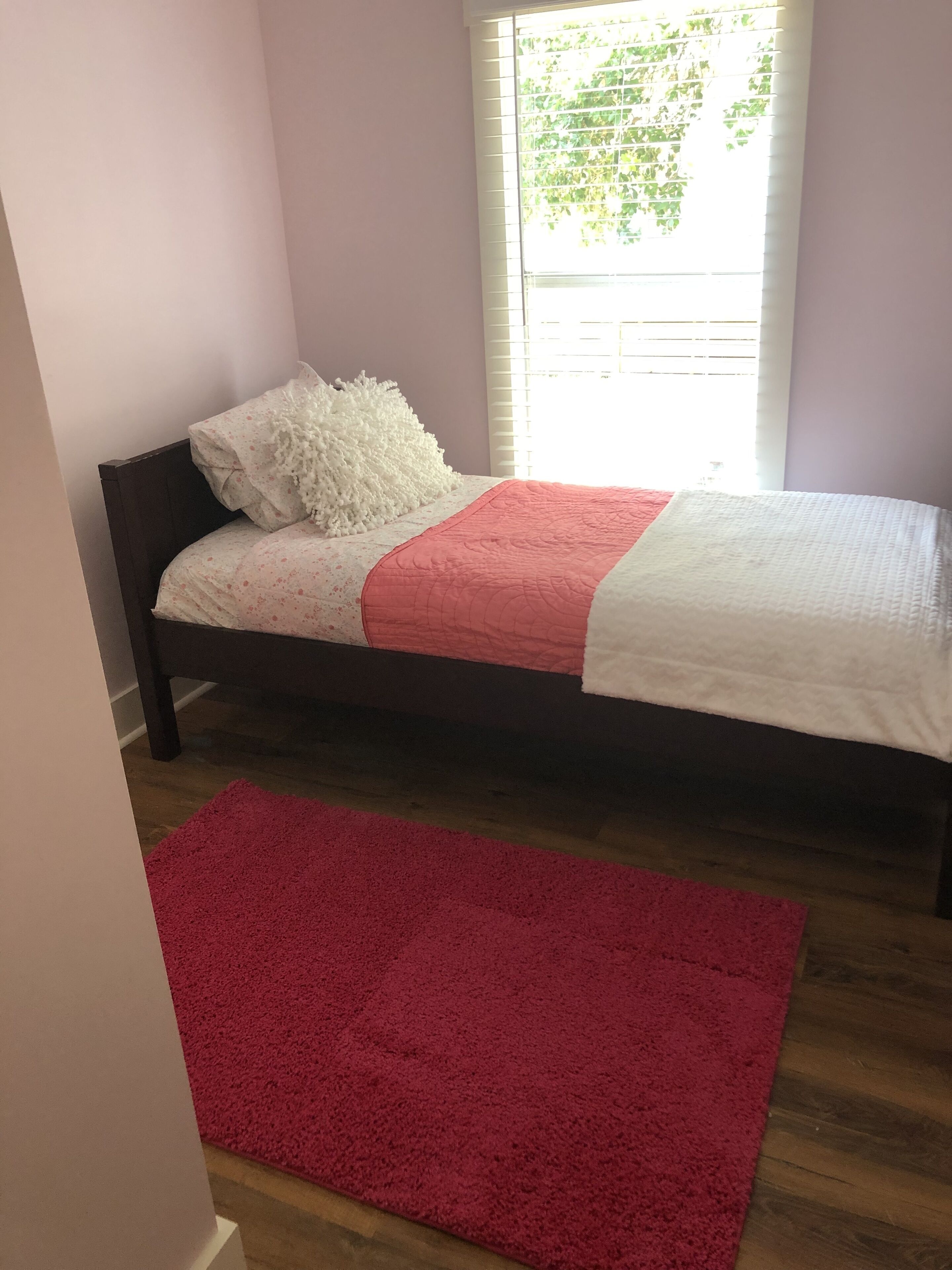 Un dormitorio con cama, alfombra roja y ventana con persianas.