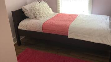 Un dormitorio con cama, alfombra roja y ventana con persianas.