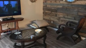 A living room with a TV, a glass coffee table, a sofa, and a wooden wall with a mirror. - LOTS of parking for vehicles and boats. Large porch with swing and table, chairs (Steinhatchee)