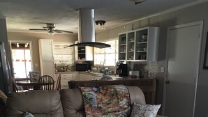 A living room with a brown leather sofa, a round coffee table, and a dining area in the background. - LOTS of parking for vehicles and boats. Large porch with swing and table, chairs (Steinhatchee)