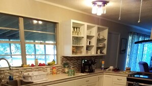 A kitchen with white cabinets, a wooden dining table, and a window with a view of trees. - LOTS of parking for vehicles and boats. Large porch with swing and table, chairs (Steinhatchee)