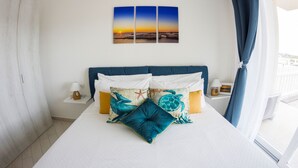 Une chambre d’hôtel avec un lit, deux tables de chevet, une fenêtre avec des rideaux et un mur orné de trois tableaux représentant des couchers de soleil.