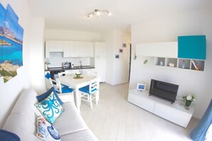 Ein modernes Wohnzimmer mit einem weißen Sofa, einem Flachbildfernseher und einem Essbereich mit weißem Tisch und Stühlen.