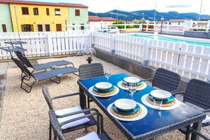 Una terraza en la azotea con una mesa de comedor para cuatro personas, rodeada de sillas de mimbre y una piscina al fondo.