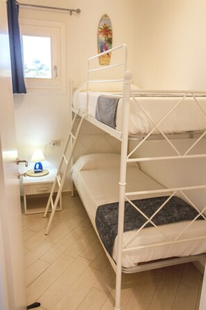 Una cama litera con escalera, una mesita de noche con lámpara y una ventana con cortinas.