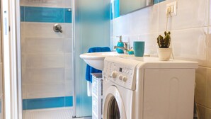 Une salle de bain moderne avec une douche à parois de verre, un lave-linge blanc, un lavabo et une plante en pot.