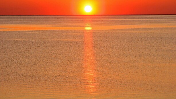 Un coucher de soleil sur une mer calme, avec un horizon dégagé.
