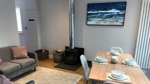 A modern living room with a sofa, a dining table set for four, a fireplace, and a framed picture on the wall. - Romantic Lodge on the Pilgrims way, Hollingbourne nestled in the Northdowns (Hollingbourne)