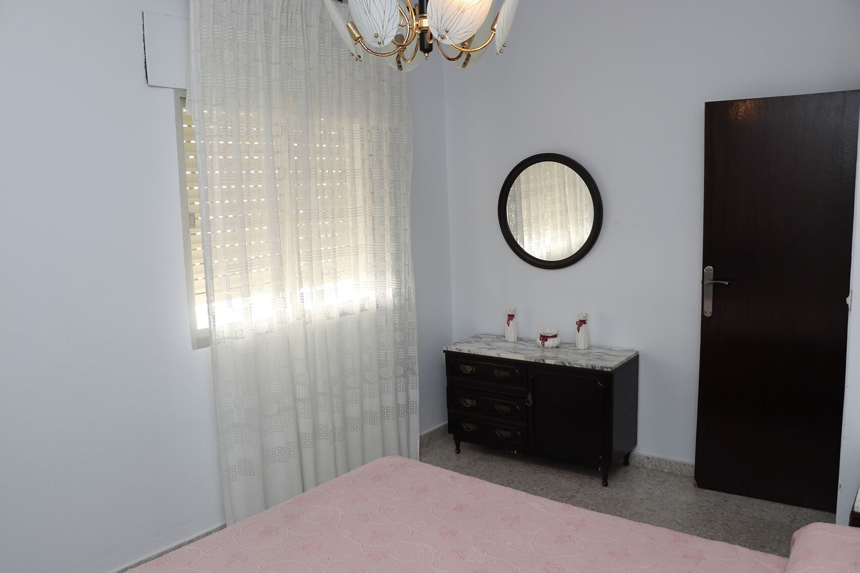 Ein Schlafzimmer mit Bett, Kommode, Spiegel und Tür.