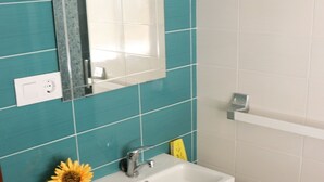 A bathroom with teal tiles, a white sink, a mirror, and a woven basket. - Central apartment on the first floor (CONIL DE LA FRONTERA)