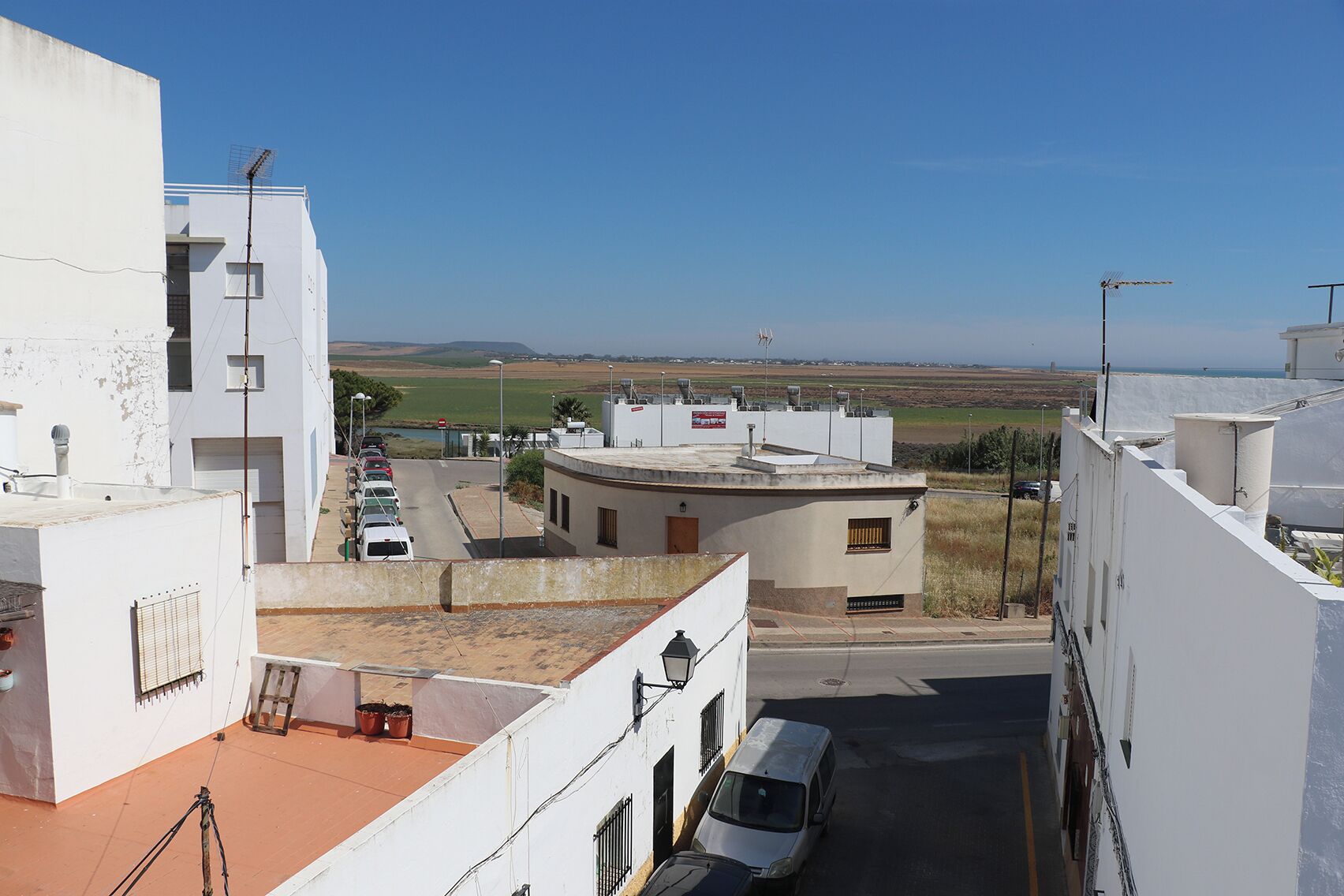 Eine schmale Straße mit Häusern an beiden Seiten, ein geparkter Transporter und ein freier Blick auf die entfernte Landschaft.