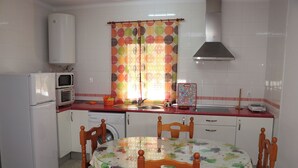 A compact kitchen with a refrigerator, microwave, and washing machine. There's a dining table with chairs, and a window with a colorful curtain. - Central apartment on the first floor (CONIL DE LA FRONTERA)