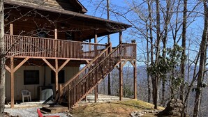 Een houten chalet met een balkon en terras, omringd door bomen en een heldere lucht.