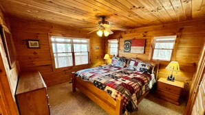 Een slaapkamer in een houten hutje, met een bed, twee nachtkastjes, een plafondventilator en een raam.