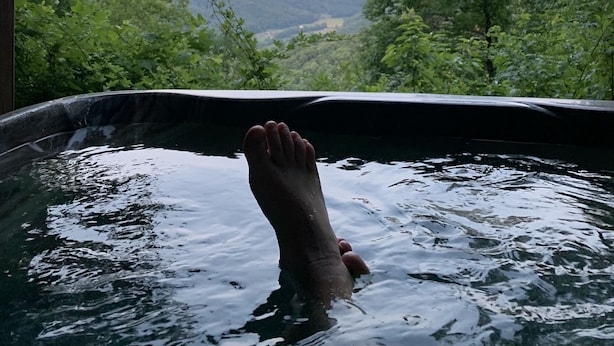 Een voet in een hottub met uitzicht op een bos en bergen.