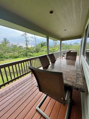 Ein überdachter Außenbereich mit Holzterrasse, Metallstühlen und einem Tisch.