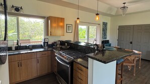 A modern kitchen with wooden cabinets, a central island, and pendant lighting. - Come & stay with us at the beautiful & peaceful Bird's Nest (Keaau)