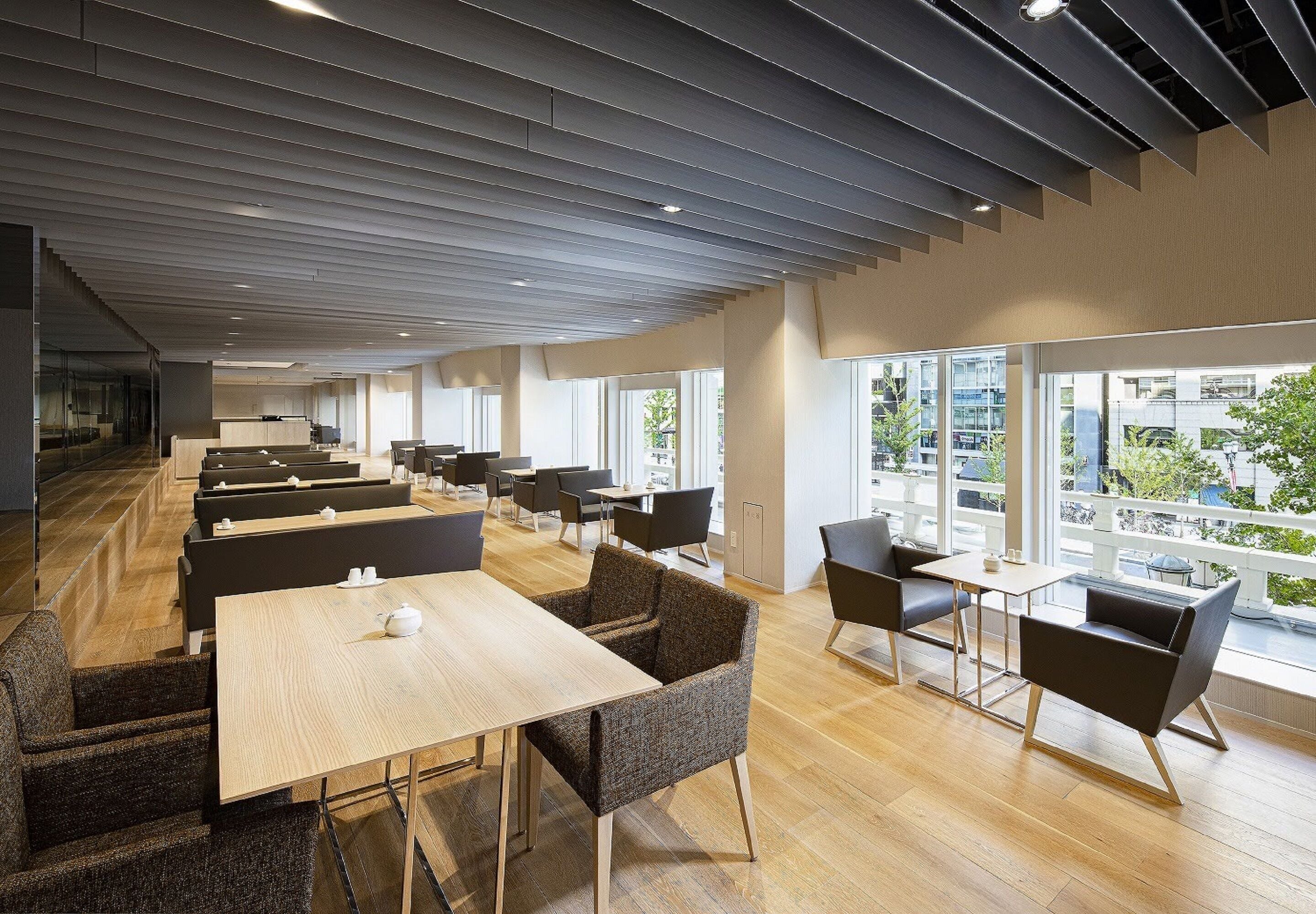 Un comedor moderno con mesas y sillas de madera, y grandes ventanales con vistas a la ciudad.