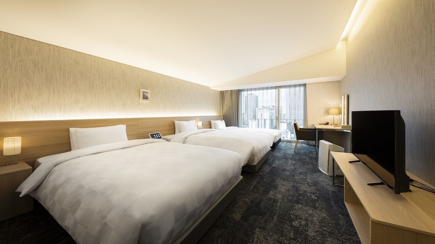 A hotel room with two beds, a desk, a TV, and a city view.