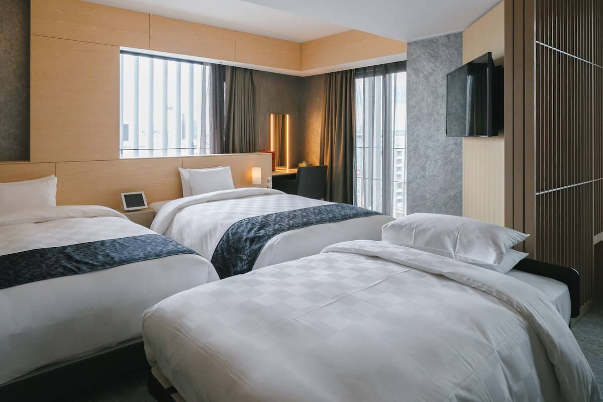 A hotel room with two beds, a desk, a TV, and a window with curtains.