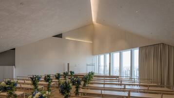 An indoor space with rows of wooden benches and a large window with curtains.