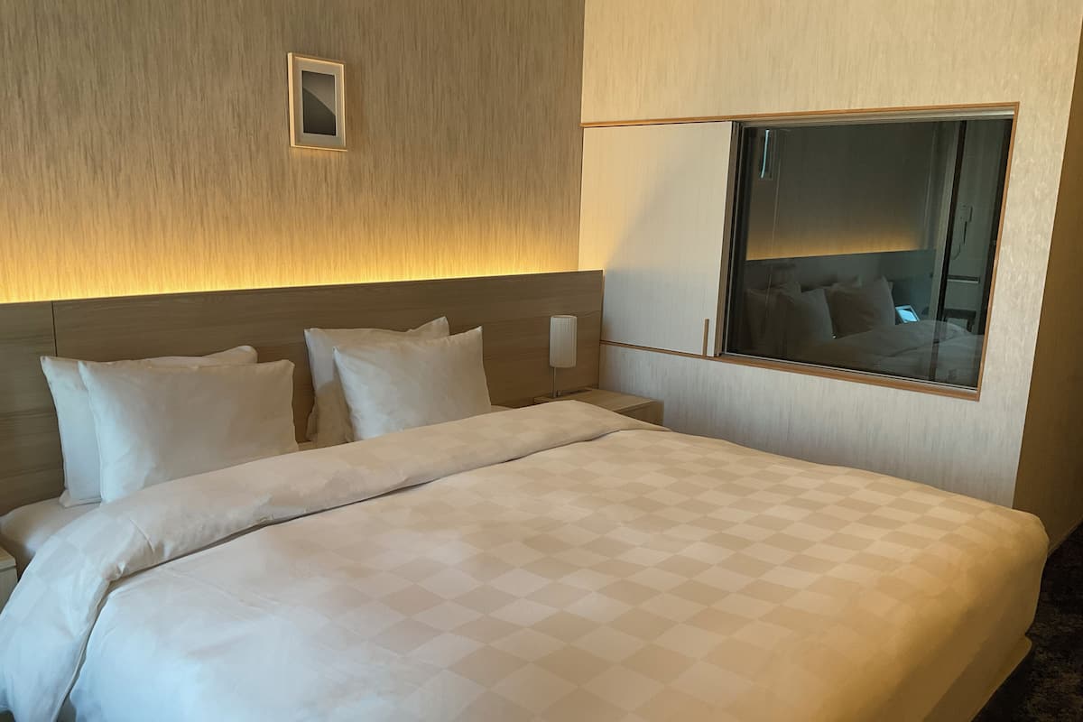 A hotel room with a large bed, a nightstand, a bedside lamp, a mirror, and a small window.