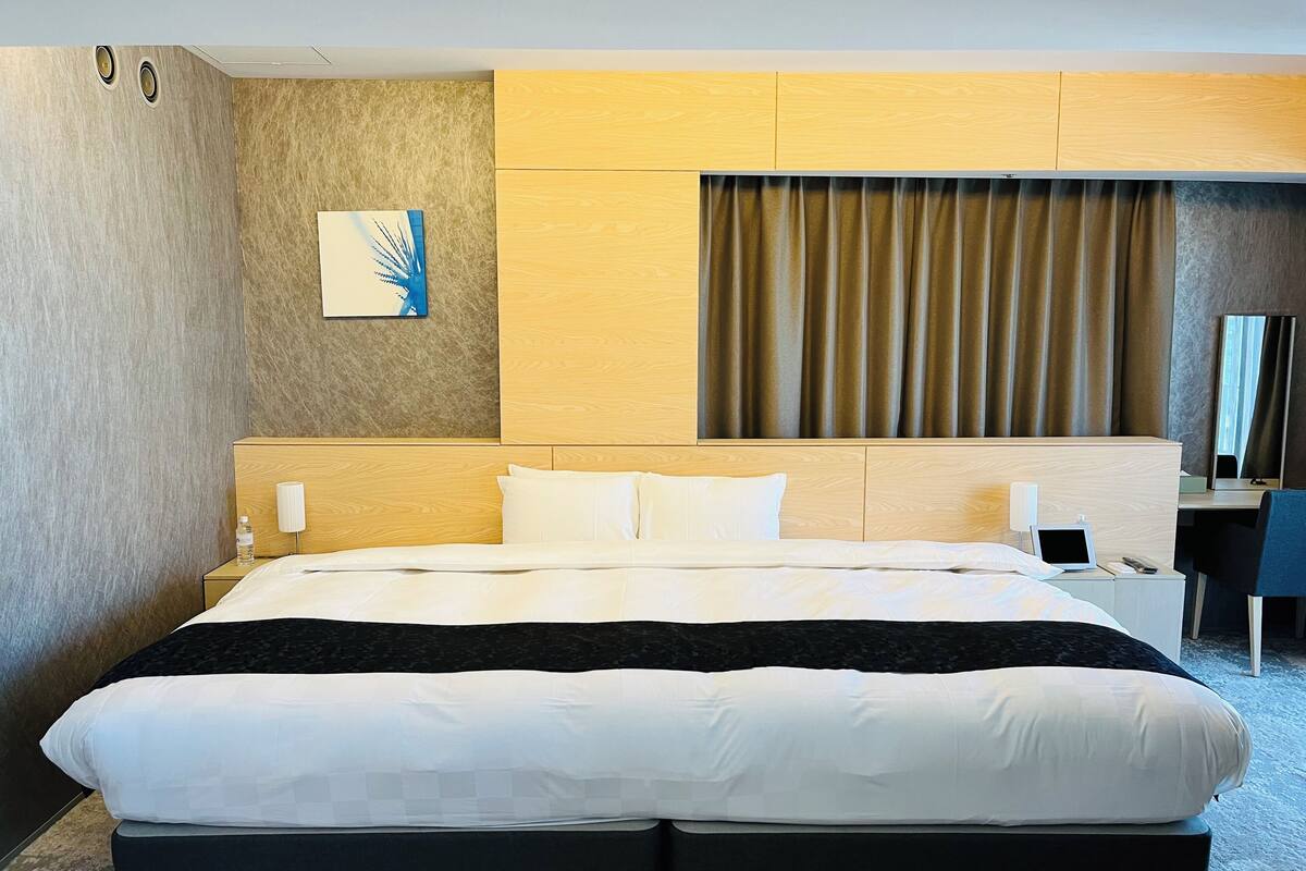 A modern hotel room with a large bed, a desk, and a view of the city.