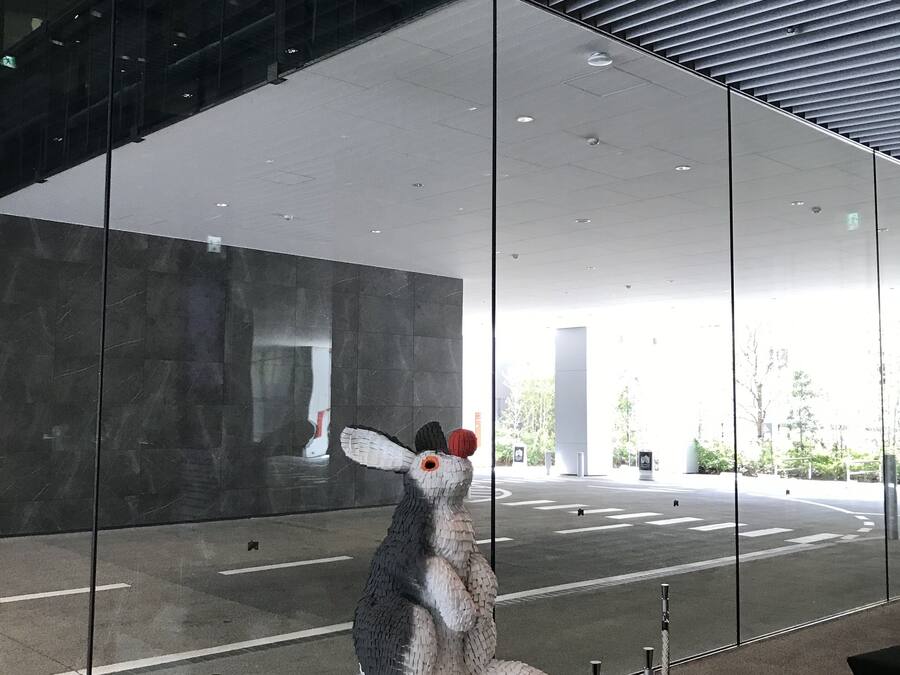 A sculpture of a rabbit on a pedestal in a modern indoor space with glass walls and a ceiling with horizontal beams.