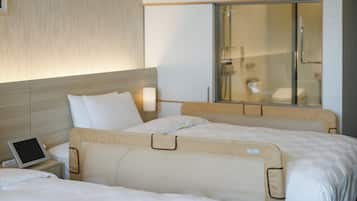 A hotel room with two beds, a bedside table with a tablet, and a large window with a view of a bathroom.