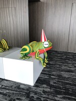 A stylized frog sculpture on a white pedestal against a wooden backdrop.