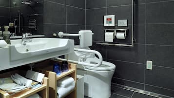 Un baño moderno con lavamanos, inodoro y bidé blancos. Hay toallas y artículos de aseo en la encimera.